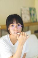 Young adult asian woman brushing teeth in font of bathroom mirror. photo