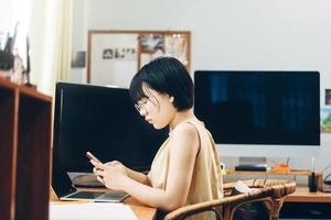 una mujer asiática adulta joven se queda y trabaja desde casa usando una aplicación de teléfono inteligente para telesalud a través de Internet en línea. foto