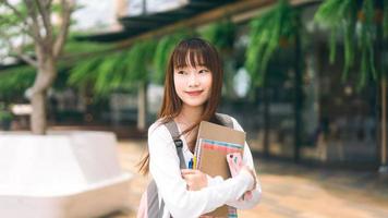 Portrait of young adult asian college student woman with notebook on day in the city. photo