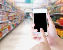 hand holding mobile phone with supermarket shelves aisle blurred background