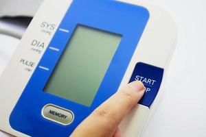 Dedo presionando el botón del monitor de presión arterial digital sobre fondo blanco. foto
