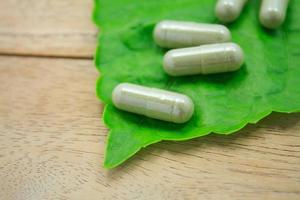 Cápsulas de hierbas medicinales con hoja de hierba verde sobre mesa de madera foto