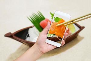 Female hand taking photo of sashimi sushi set