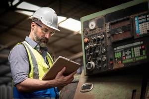 ingeniero o técnico caucásico con uniforme de seguridad trabajando y comprobando la información de mantenimiento en línea de la máquina en la tableta. foto