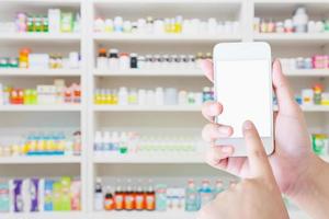 Una farmacéutica sostiene un teléfono inteligente móvil en la farmacia.