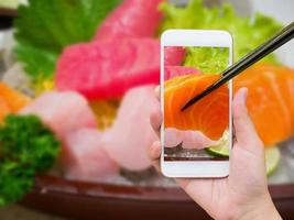 Female hand taking photo of sashimi sushi set