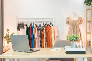 Online clothing store with laptop, notebook, clothing rack, mannequin and object decoration on desk in home office photo