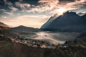 Aerial view of sunrise over mountain range with foggy and local traditional village on hill in tropical rainforest at national park