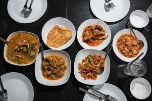 Variety of Thai food with spicy soup, fried fish, tofu, chicken curry, salad and silverware on dining table at dinner photo