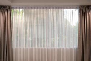 Open beige curtain with light filter fabric on window photo