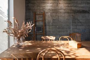 Interior of living room with wooden table, chair, dry leaf in glass wave, tissue box and wooden stair on concrete wall photo