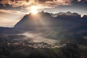 Aerial view of sunrise over Doi Luang Chiang Dao mountain range with foggy and local village on hill in tropical rainforest at Ban Na Lao Mai