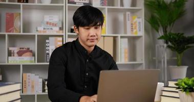 un joven empresario asiático aburrido trabaja en una laptop en una oficina moderna. gerente aburrido navegando en internet. hombre cansado usando computadora portátil en la oficina en casa. hombre navegando con pc. video