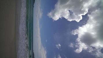 video vertical pov playa de arena oceánica y textura de la superficie del agua. olas espumosas con cielo y nubes. hermosa playa tropical y palmeras. increíble costa de arena con olas de mar blanco. concepto de naturaleza.