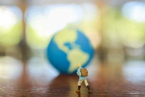 Travelling concepts. Traveler miniature miniature people figure with backpack walking on wooden table with mini world ball map as background with copy space. photo