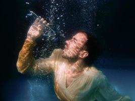 una toma submarina de un hombre bebiendo agua en una piscina con fondo negro