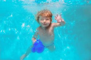 linda sonriente adorable niña buceando en la piscina azul submarina. estilo de vida activo, lección de natación infantil. actividad de deportes acuáticos durante las vacaciones familiares de verano en un resort tropical