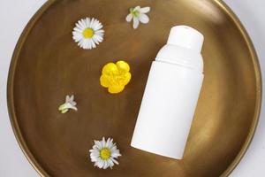 White cosmetic container on copper plate with flowers, mockup photo