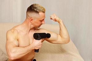 Sport man using massage gun at home photo