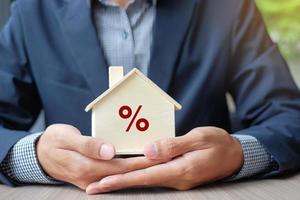 Businessman hands holding wooden House model with Percentage sign. Interstate rate, Property insurance and real estate concepts photo