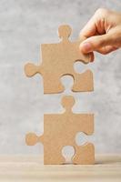 Man connecting couple puzzle piece, wood jigsaw on table. Business solutions, mission, success, goals and strategy concepts photo