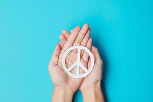 International Day of Peace. Hands holding white paper Peace symbol on blue background. Freedom, Hope, World Peace day 21 September and Nuclear Disarmament concepts. photo