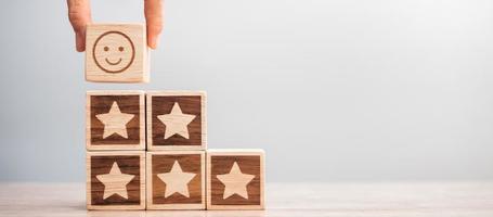 hand holding smile face over Star symbol blocks on table background. Service rating, ranking, customer review, satisfaction, evaluation and feedback concept photo