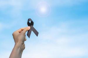 Melanoma and skin cancer, Vaccine injury awareness month and rest in peace concepts. man holding black Ribbon on sky background photo