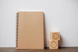 emotion face block and notebook on table. Emoticon for customer review, satisfaction, mood, mental health and feedback concept photo