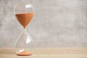 Hourglass on table, Sand flowing through the bulb of Sandglass measuring the passing time. countdown, deadline, Life time and Retirement concept photo