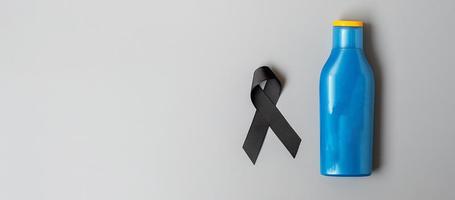 Melanoma and skin cancer awareness month. black Ribbon and body sunscreen bottle on grey background. World cancer day concept photo