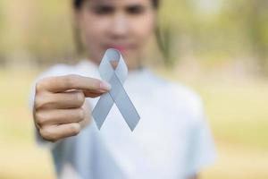 mes de concientización sobre el cáncer cerebral, mano de mujer sosteniendo una cinta de color gris para apoyar a las personas que viven. concepto de salud y día mundial del cáncer foto