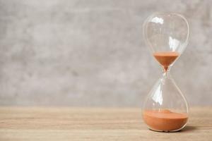 Hourglass on table, Sand flowing through the bulb of Sandglass measuring the passing time. countdown, deadline, Life time and Retirement concept photo