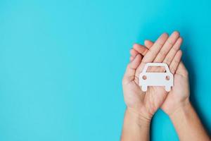 Hand holding paper Car cutout on blue background. Vehicle insurance, warranty, Automobile rental, Transportation, Maintenance and repair concept photo