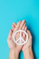Dia Internacional de la Paz. manos sosteniendo el símbolo de paz de papel blanco sobre fondo azul. libertad, esperanza, día mundial de la paz 21 de septiembre y conceptos de desarme nuclear. foto