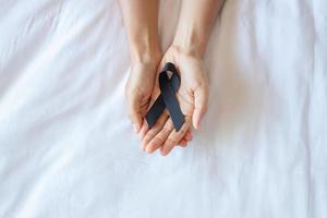 Melanoma and skin cancer, Vaccine injury awareness month and rest in peace concepts. Man holding black Ribbon on white bed background photo