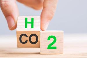 voltear a mano bloques de cubos de madera con dióxido de carbono co2, cambiar a texto de hidrógeno h2 en el fondo de la mesa. conceptos de carbono libre, energía alternativa y cambio climático global foto