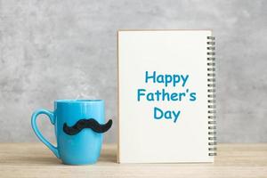 Happy Father day with paper notepad, Blue coffee cup or tea mug and Black mustache decor on table. International men day and celebration concept photo