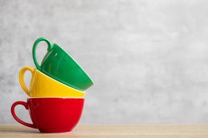 pila de coloridas tazas de café en el fondo de la pared en el café. taza de cerámica de color verde, amarillo y rojo en la mesa en casa. concepto del día internacional del café foto