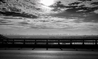 Black and white toned view from the bridge of city near the river and sky and white clouds. Sad, hopeless and death background. City air pollution and global warming concept. Bad air quality. photo