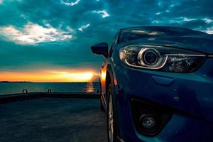 Blue compact SUV car with sport and modern design parked on concrete road by the sea at sunset in the evening. Hybrid and electric car technology concept. Car parking space. Automotive industry. photo