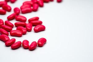 Selective focus of red kidney shape sugar coated tablet pills on white background with copy space photo