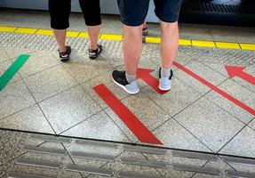 pasajero parado en la plataforma ferroviaria esperando abordar el tren eléctrico de alta velocidad en la estación de metro. transporte ferroviario moderno. turista de pie en el signo de flecha roja de pintura de piso. estilo de vida de viaje urbano foto