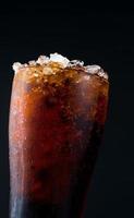 Soft drink with ice in glass isolated on dark background with copy space. There is a drop of water on the transparent glass surface. photo