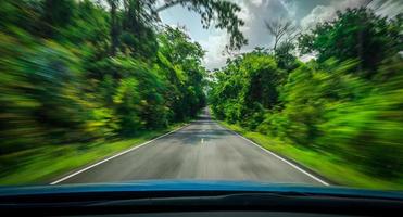 vista desde la parte delantera del coche azul en la carretera de asfalto y el desenfoque de movimiento de velocidad en la carretera en verano con el bosque de árboles verdes en el campo foto