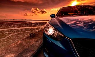 Blue compact SUV car with sport and modern design parked on concrete road by the sea at sunset. Environmentally friendly technology. Business success concept. Car with open headlamp light. photo