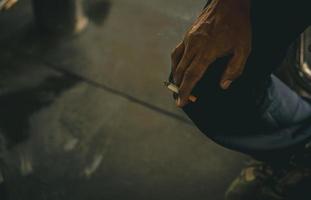 Asian man with dirty hand hold cigarette and smoke. Poor Asian men labor sit and smoking cigarette while take a break or after hard working. Nicotine addicted. Carcinogens causes lung cancer. photo