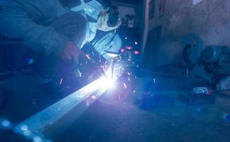 Welder welding metal with argon arc welding machine and has welding sparks. A man wears welding mask and protective gloves. Safety in industrial workplace. Welder working with safety. Steel industry. photo