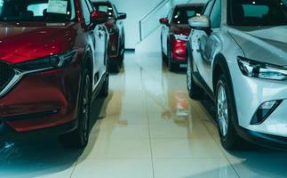 vista frontal suv rojo y auto blanco estacionado en una sala de exposición de lujo. oficina del concesionario de automóviles. coche nuevo aparcado en la sala de exposición moderna. negocio de venta y alquiler de autos. arrendamiento de automóviles y antecedentes de seguros. foto