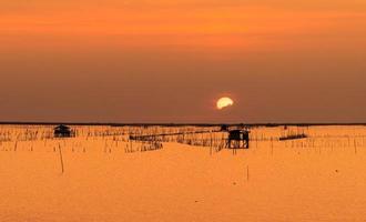 hermoso cielo de puesta de sol sobre el mar por la noche. el sol está oscurecido por algunas nubes al atardecer. choza de pescador de pesca costera en tailandia. mar al anochecer. paisaje marino de silueta y cabaña en la costa. foto
